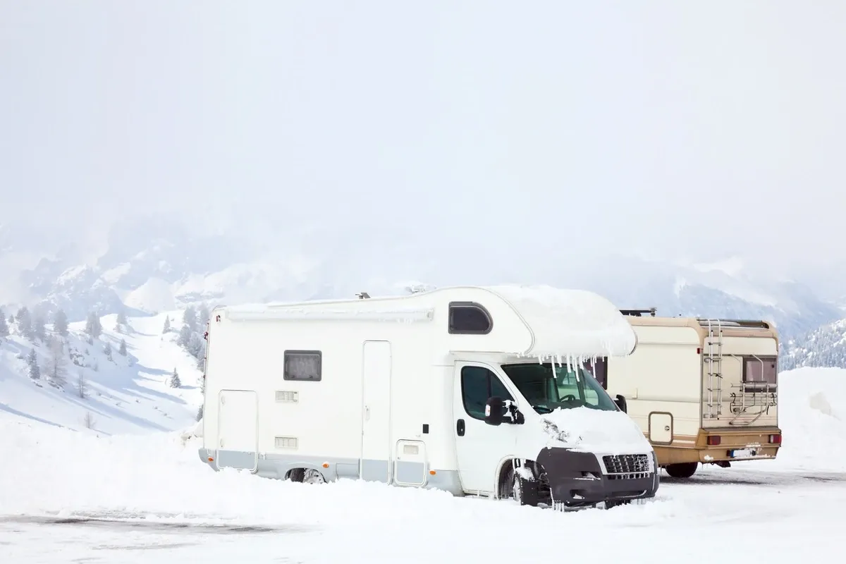 Snow-covered RVs parked in a snowy mountain area, with icicles hanging from the roof and heavy snow piled around.